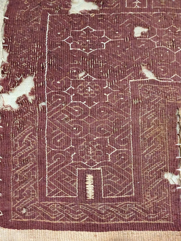 Mörkröd textil med orientaliska knutar och blommor.